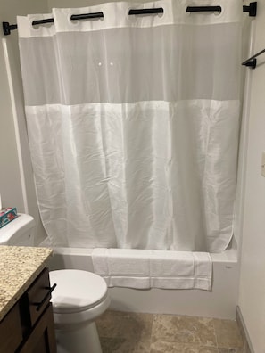 Ein Badezimmer mit weißer Duschvorhang, Toilette und einer Arbeitsplatte aus Granit.