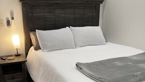 Un letto rifatto con cura, una testiera scura, una lampada da comodino e un comodino con cassetti.