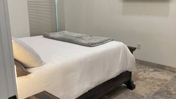 Un dormitorio con cama, una mesita de noche con control remoto, un televisor montado en la pared y un equipo de aire acondicionado.
