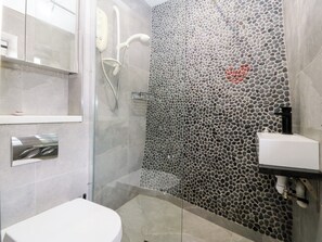 A modern bathroom with a glass-enclosed shower, a white sink, and a pebble-patterned wall. - 5 Bryn Llan (Pwllheli)