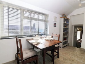 A dining area with a wooden table and chairs, a window with blinds, and a bookshelf. - 5 Bryn Llan (Pwllheli)