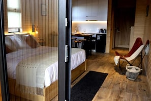 Un dormitorio con cama, una silla, escritorio y una zona de cocina.
