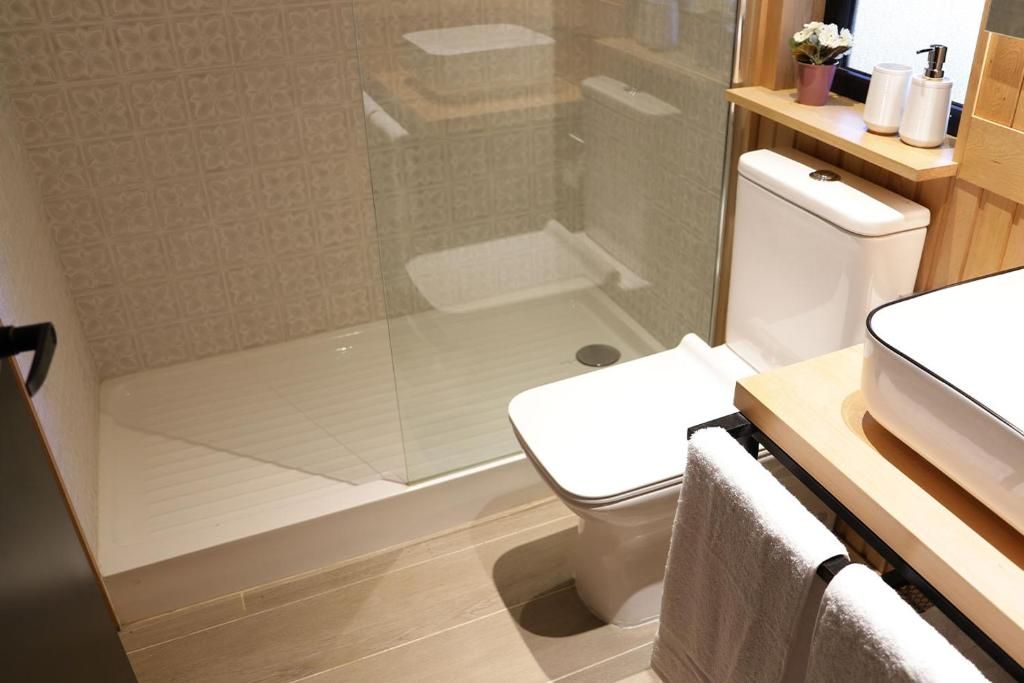 Un baño moderno con cabina de ducha de vidrio, inodoro y zona de lavamanos con toallero.