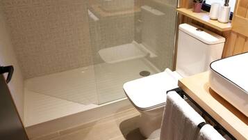 Un baño moderno con cabina de ducha de vidrio, inodoro y zona de lavamanos con toallero.