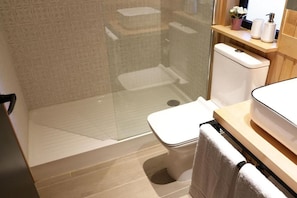 Un baño moderno con cabina de ducha de vidrio, inodoro y zona de lavamanos con toallero.