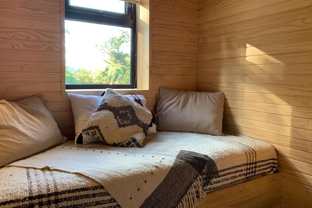 Una habitación con una cama, almohadas, un ventanal y paredes de madera.