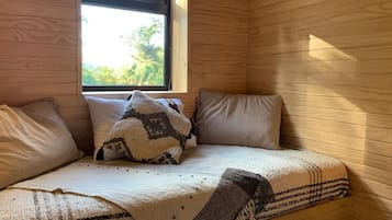 Una habitación con una cama, almohadas, un ventanal y paredes de madera.