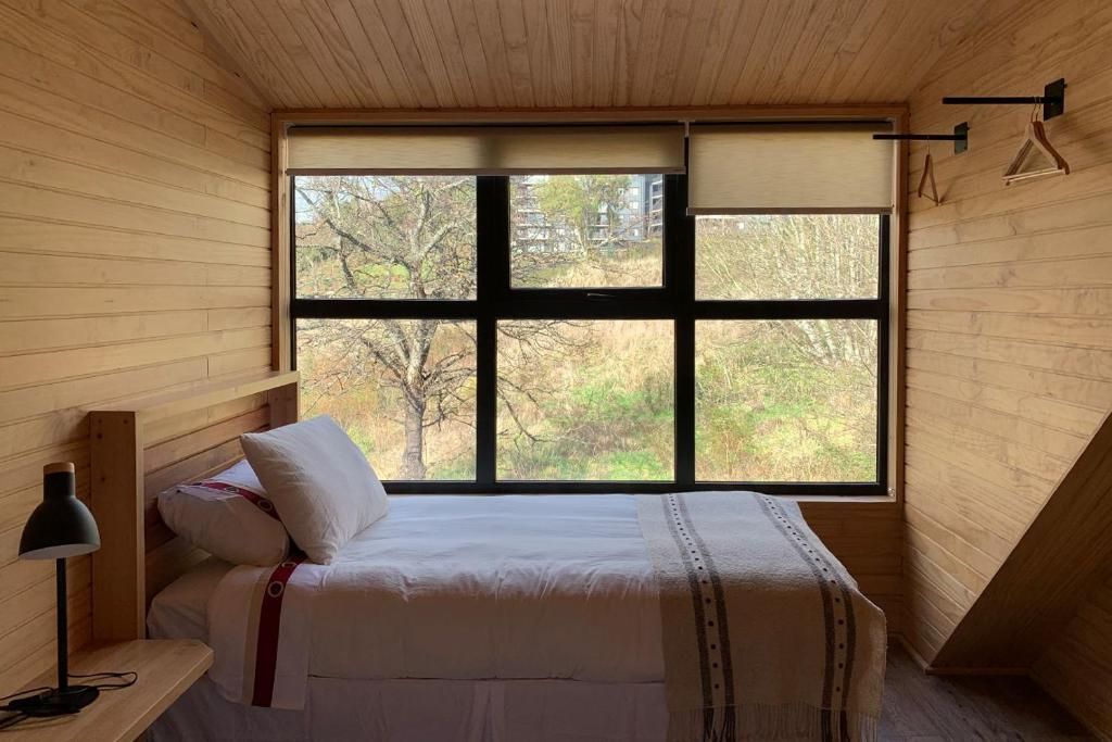 Une chambre à coucher avec un lit, une lampe de chevet et une fenêtre donnant sur des arbres et des immeubles.
