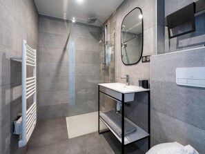 A modern bathroom with a glass-enclosed shower, a white sink, and a towel rack.