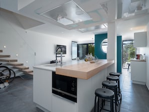 A modern kitchen with a central island, bar stools, and a bicycle in the background.