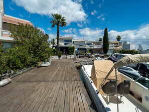 A wooden deck with boats, a covered area, and a building with balconies in the background.
