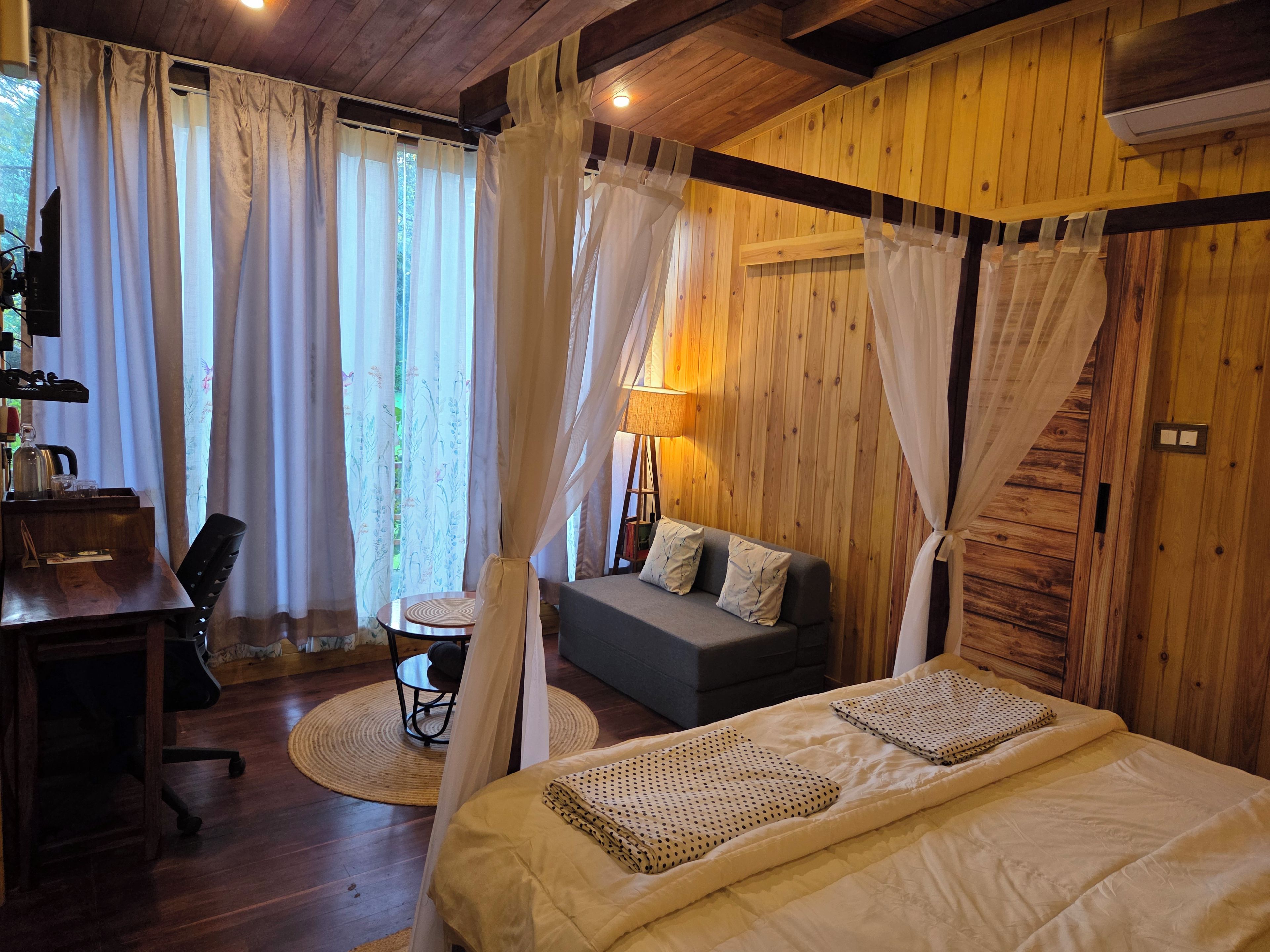 A room with a bed, a desk, a chair, a sofa, and a lamp.