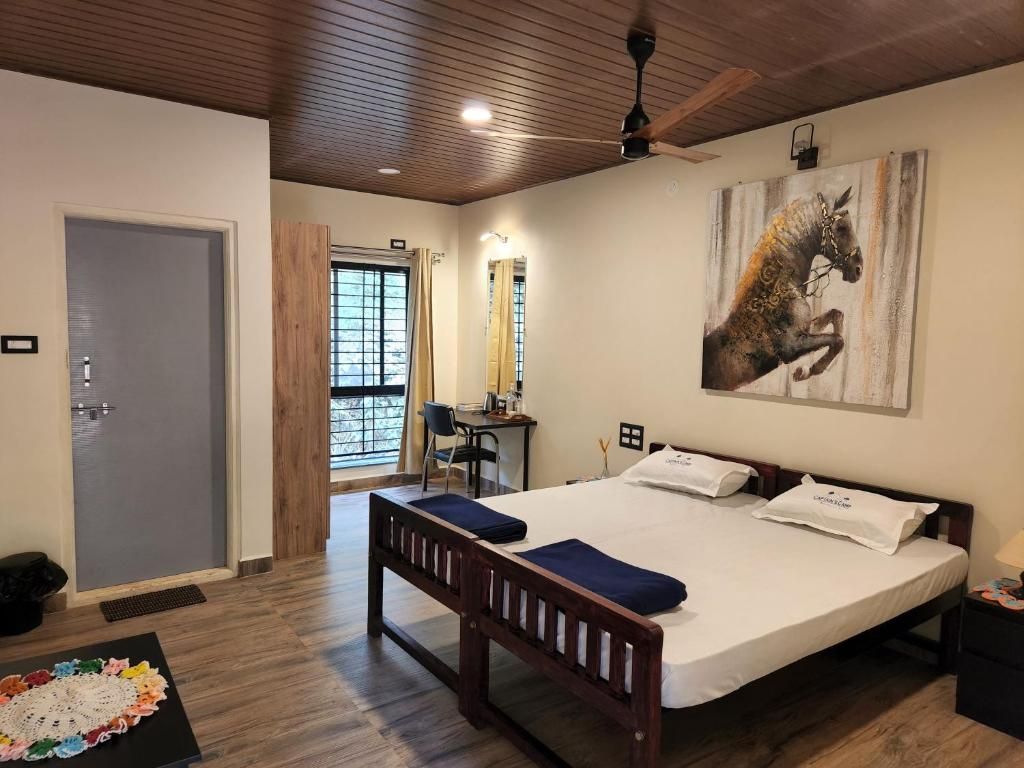 A hotel room with a large bed, a desk, a chair, and a ceiling fan.