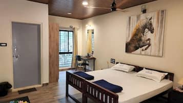 A hotel room with a large bed, a desk, a chair, and a ceiling fan.