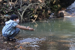A person crouching by a river with water splashing around. - Captain's Camp (Sirsi)