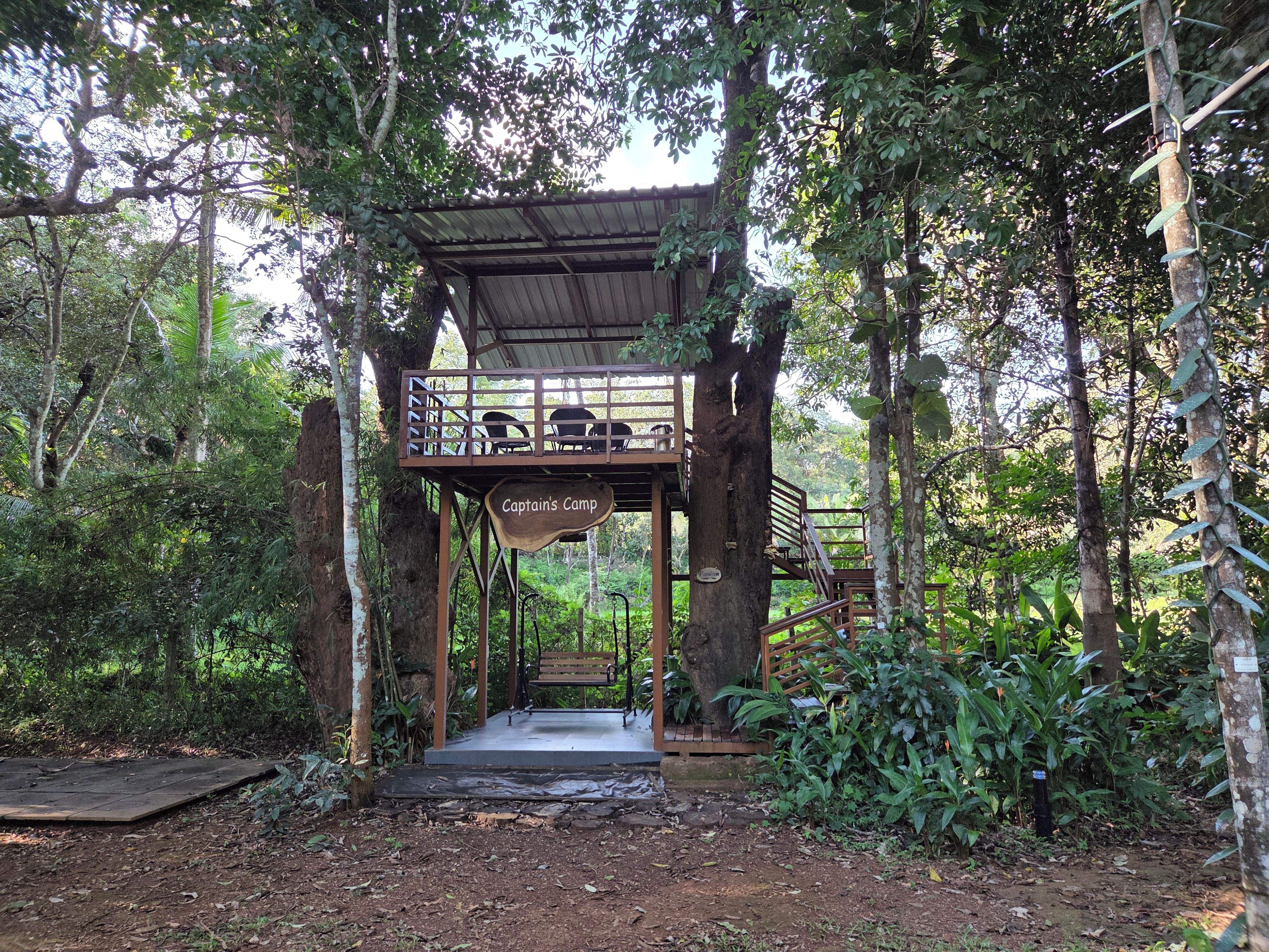 A wooden structure labeled 'Captains Camp' with a bench and tables, surrounded by trees and vegetation.