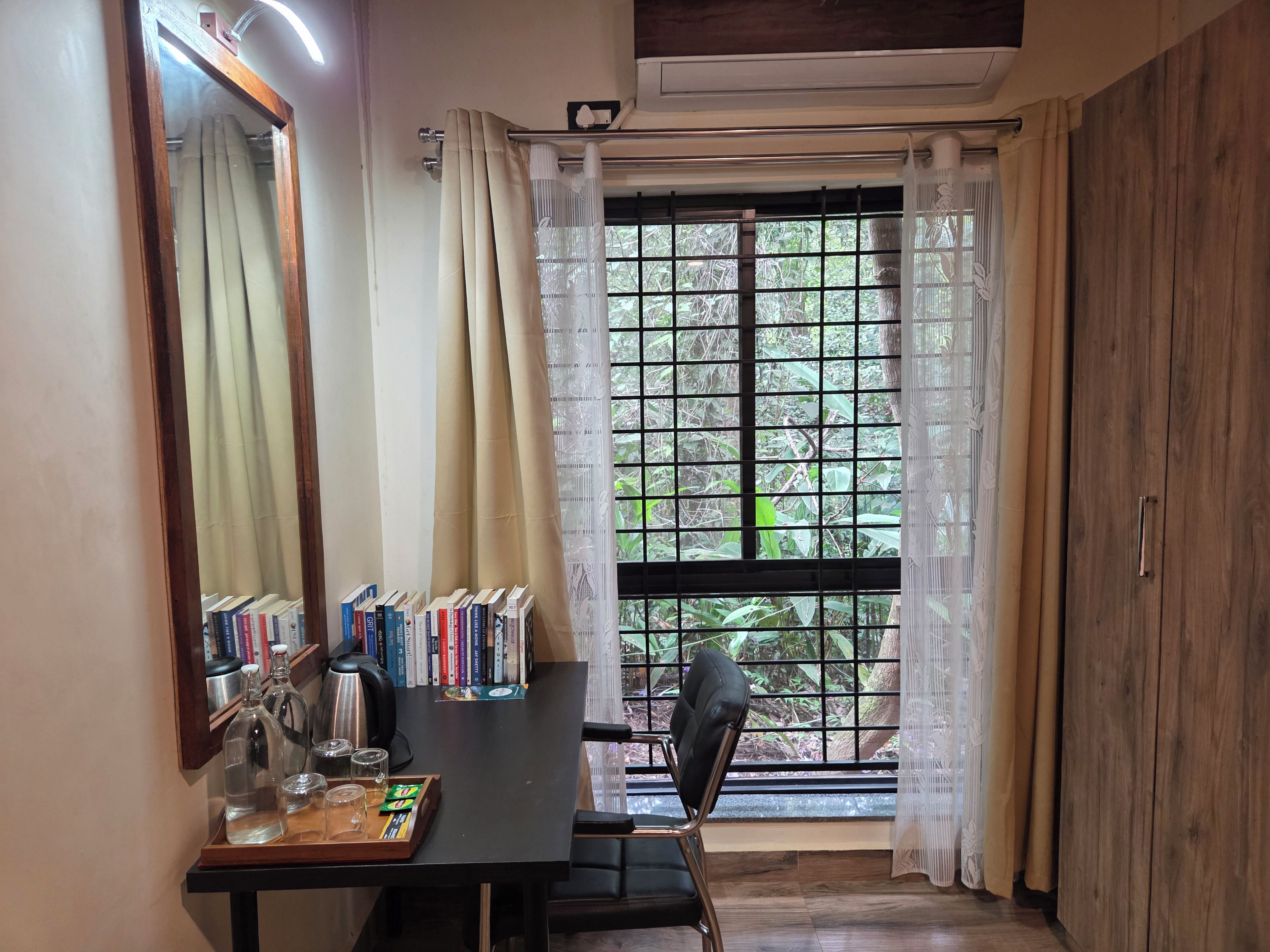 A room with a large window, a desk with books, a chair, and a mirror.
