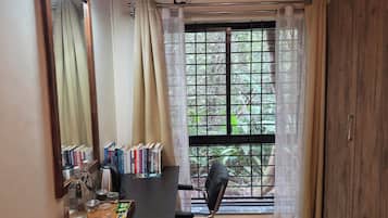 A room with a large window, a desk with books, a chair, and a mirror.