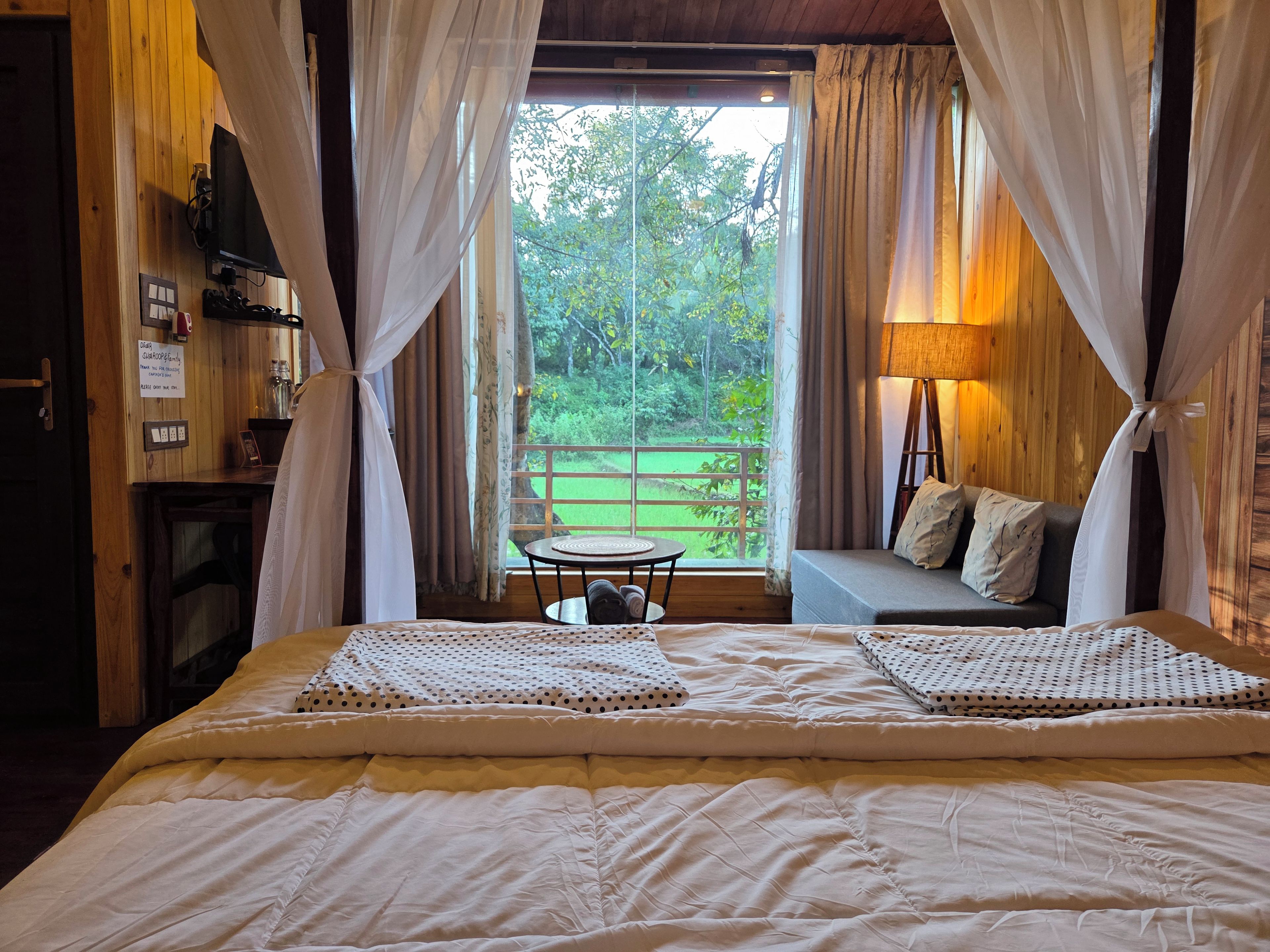 A bedroom with a bed, a sofa, a table, and a view of a green landscape through the window.