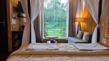 A bedroom with a bed, a sofa, a table, and a view of a green landscape through the window.