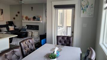 A dining area with a table set for four, a sofa, a TV, and a cross on the wall.