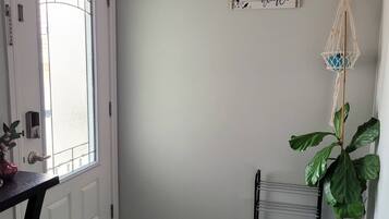 A room with a white door, a welcome sign, a macrame wall hanging, and a large green plant.