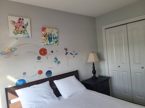 A bedroom with a bed, nightstand, lamp, and wall decorations including a planet mural and a 'Wild & Free' sign. - Room-charming and Cozy Home (Edmonton)