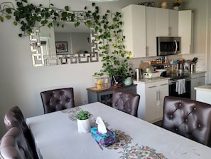 A dining area with a table, chairs, and a kitchen in the background. - Rapperswill Serenity (Edmonton)