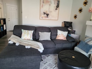 A living room with a grey sofa, patterned throw, and decorative pillows. - Rapperswill Serenity (Edmonton)