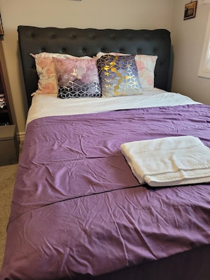 A bed with a purple bedspread, a white blanket, and multiple decorative pillows. - Rapperswill Serenity (Edmonton)