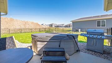 Une terrasse extérieure avec un jacuzzi, un barbecue et un espace salon.