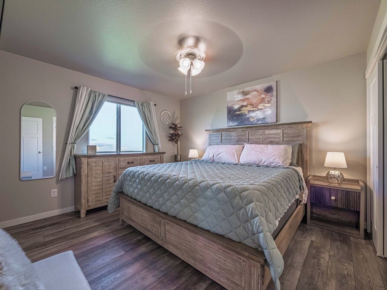 Ein Schlafzimmer mit einem großen Bett, einem Holz-Kopfteil, Nachttischlampen, einem Deckenventilator und einem Fenster mit Vorhängen.