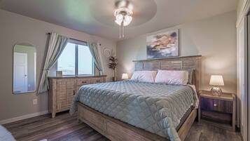 Ein Schlafzimmer mit einem großen Bett, einem Holz-Kopfteil, Nachttischlampen, einem Deckenventilator und einem Fenster mit Vorhängen.