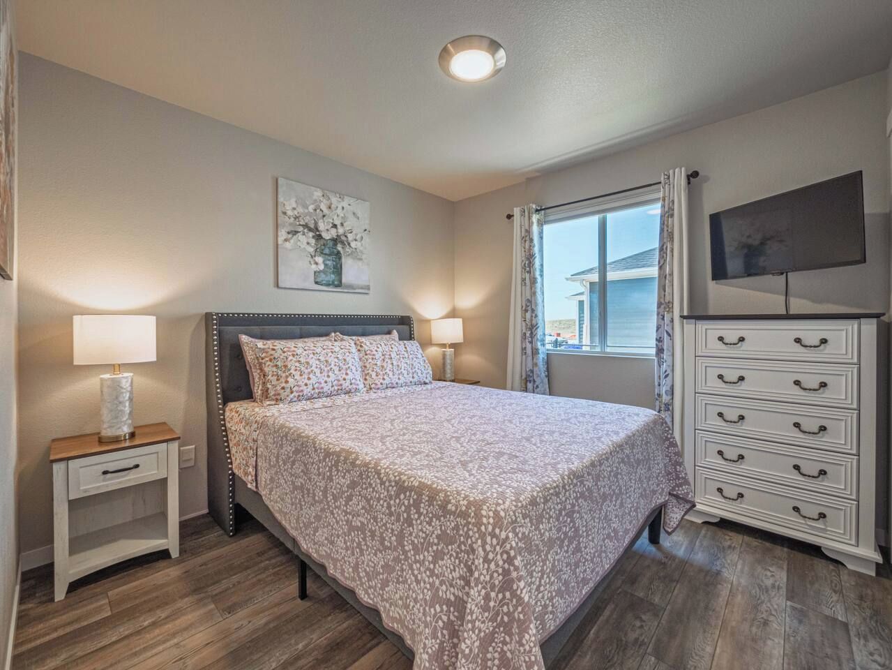 Une chambre à coucher avec un lit, des tables de chevet, une commode et une fenêtre avec des rideaux.