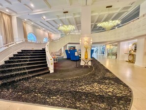 A grand hotel lobby with a central staircase, a chandelier, and a patterned carpet. - Charming 2BR/2BA Oceanfront Gem, Miami Beach (Miami Beach)