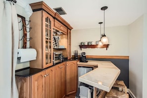 Cocina compacta con armarios de madera, horno empotrado, cafetera y lámpara colgante.
