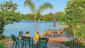 Un patio con suelo de piedra, mobiliario exterior y vistas a un lago.