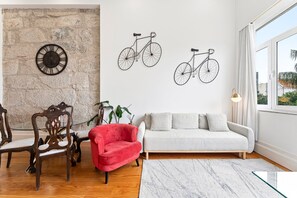 A living room with a stone wall, a red chair, a white sofa, and two wall-mounted bicycles. - GuestReady - Charming Duplex in Porto's Heart (Porto)