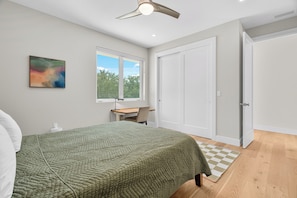 Ein Schlafzimmer mit Bett, Schreibtisch, Stuhl, Fenster und Tür.