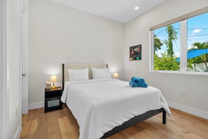 Ein Schlafzimmer mit Bett, Nachttischen, einem Fenster mit Blick und einem Wandbild.