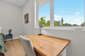 Ein Zimmer mit Schreibtisch aus Holz, einem Stuhl, einem kleinen Tisch mit einer Vase und einem Bild an der Wand.