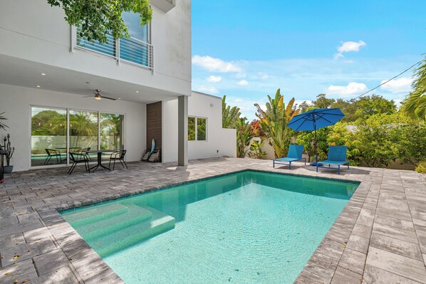 Ein moderner Außenpool mit glasklar blauem Wasser, umgeben von einer gepflasterten Terrasse.