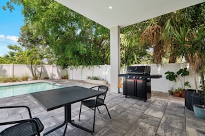 Eine Terrasse mit Pool, Grill und Gartenmöbeln.