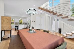 Eine moderne Küche mit weißen Schränken, ein Essbereich mit einem langen Tisch und eine Treppe, die in eine obere Etage führt.
