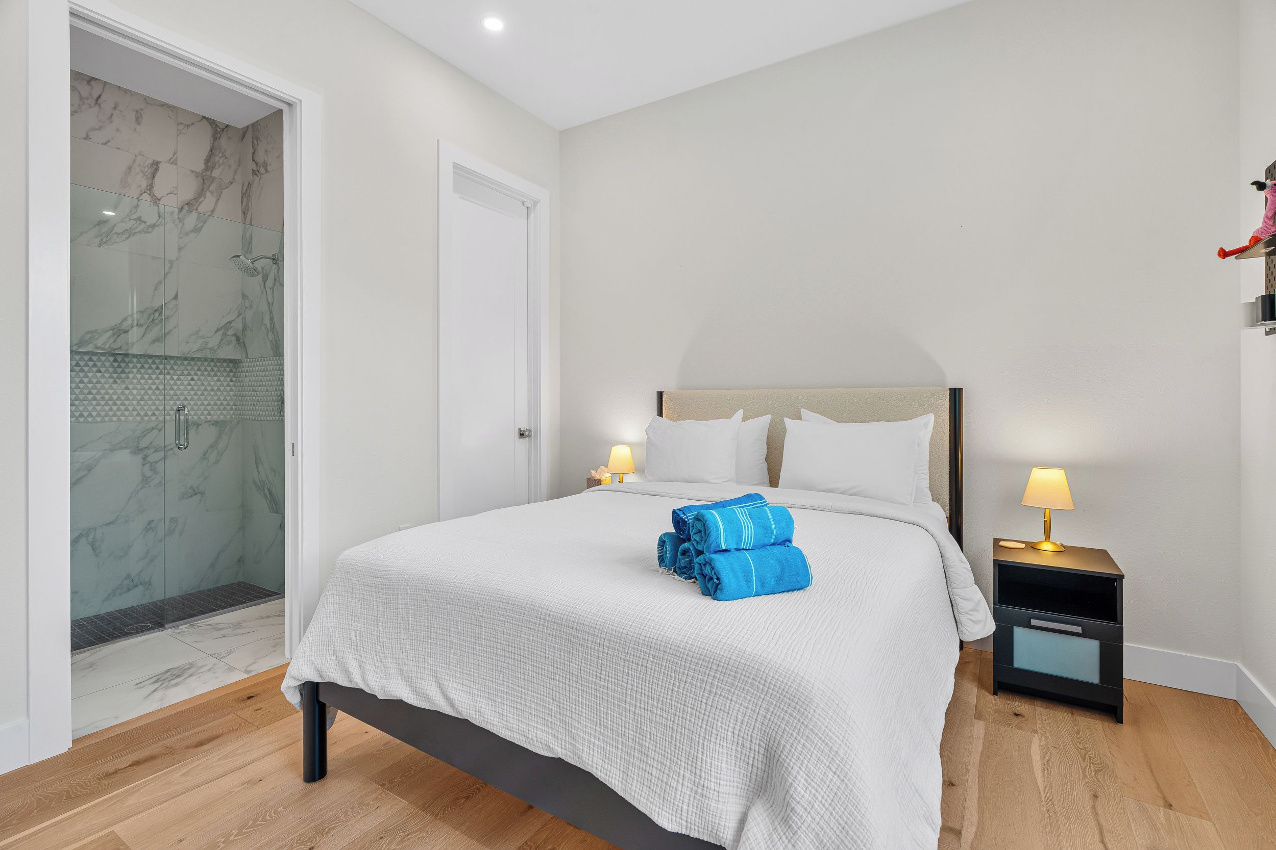 A hotel room with a bed, a nightstand, a lamp, a shower with marble walls, and a door.