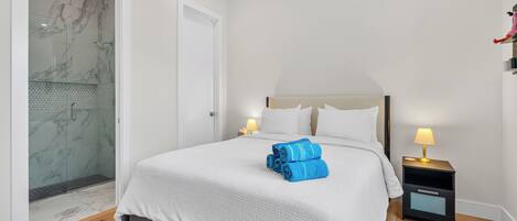 A hotel room with a bed, a nightstand, a lamp, a shower with marble walls, and a door.