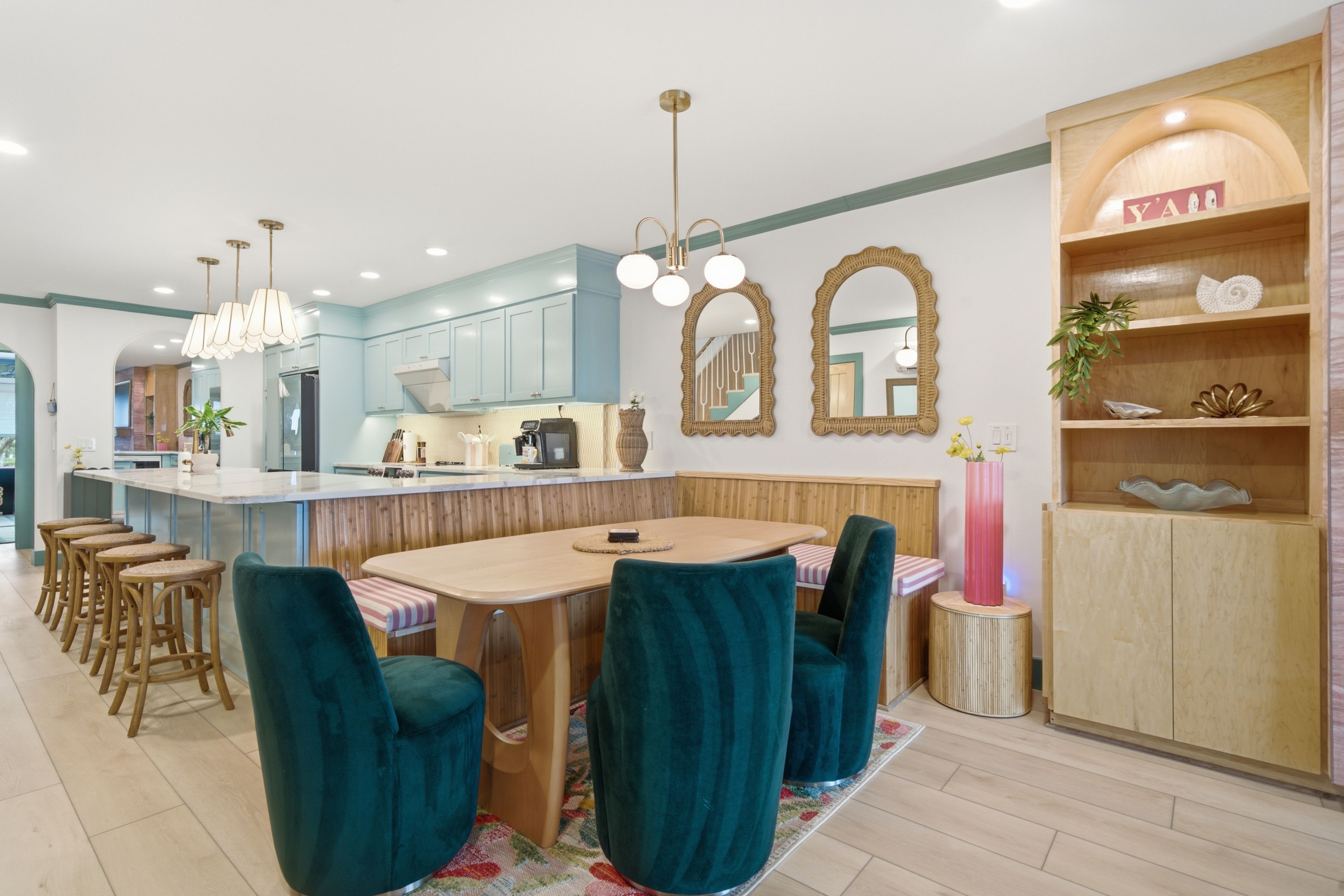 A modern kitchen with a central island, bar stools, and a dining area with a round table and teal chairs.