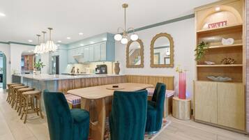 A modern kitchen with a central island, bar stools, and a dining area with a round table and teal chairs.