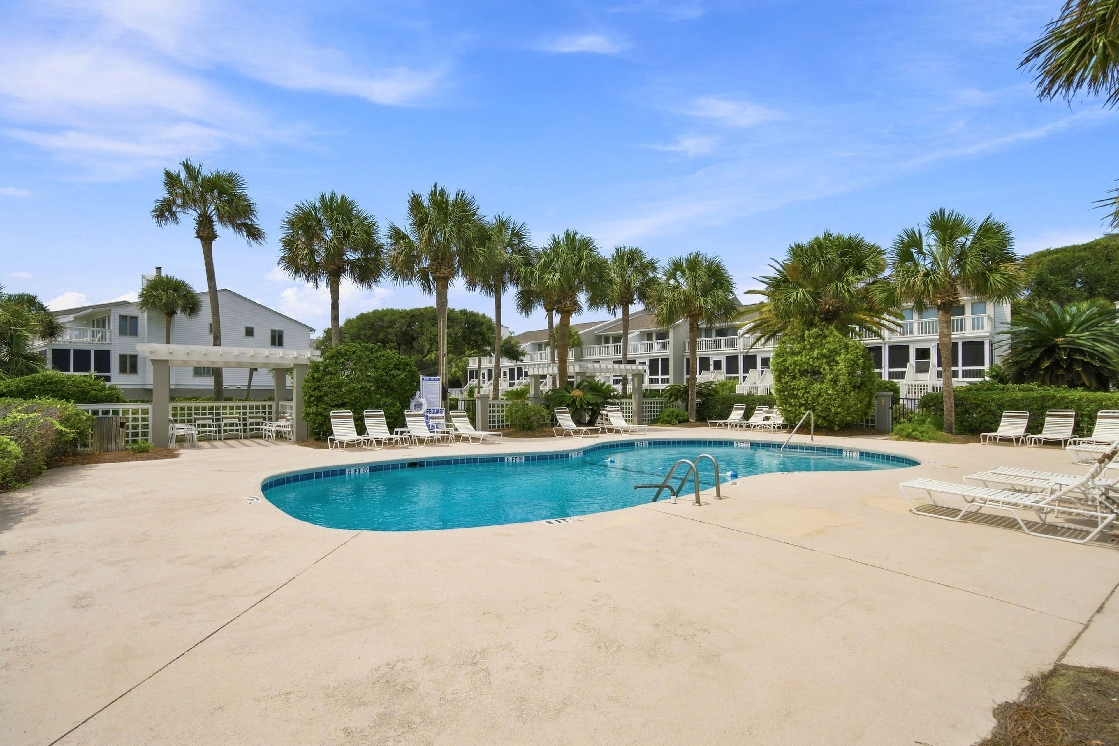A swimming pool with lounge chairs, surrounded by palm trees and a clear sky.