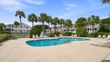 A swimming pool with lounge chairs, surrounded by palm trees and a clear sky.